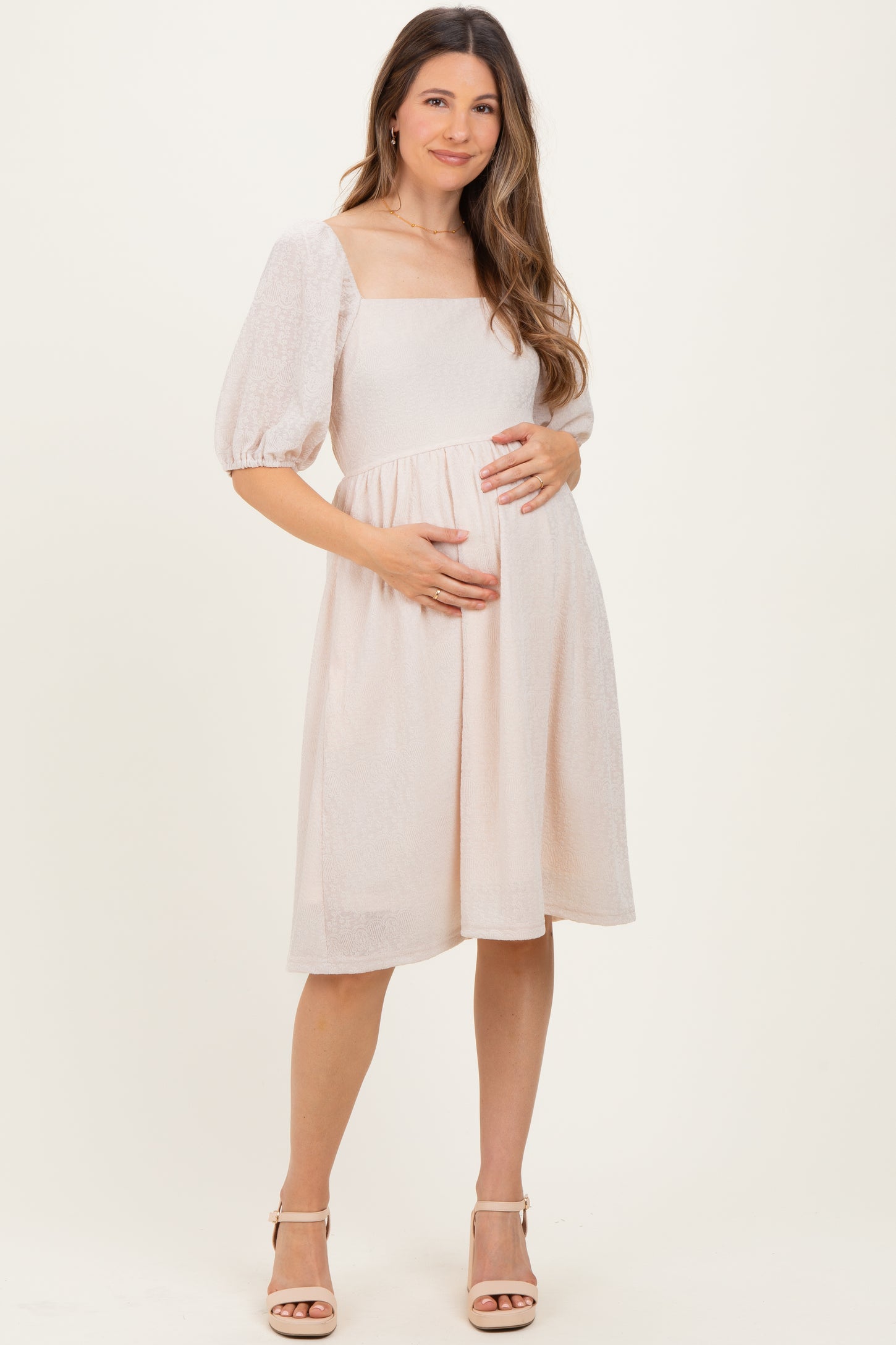 woman wearing a light pink maternity dress with puff sleeves, holding her baby bump