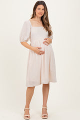 woman wearing a light pink maternity dress with puff sleeves, holding her baby bump