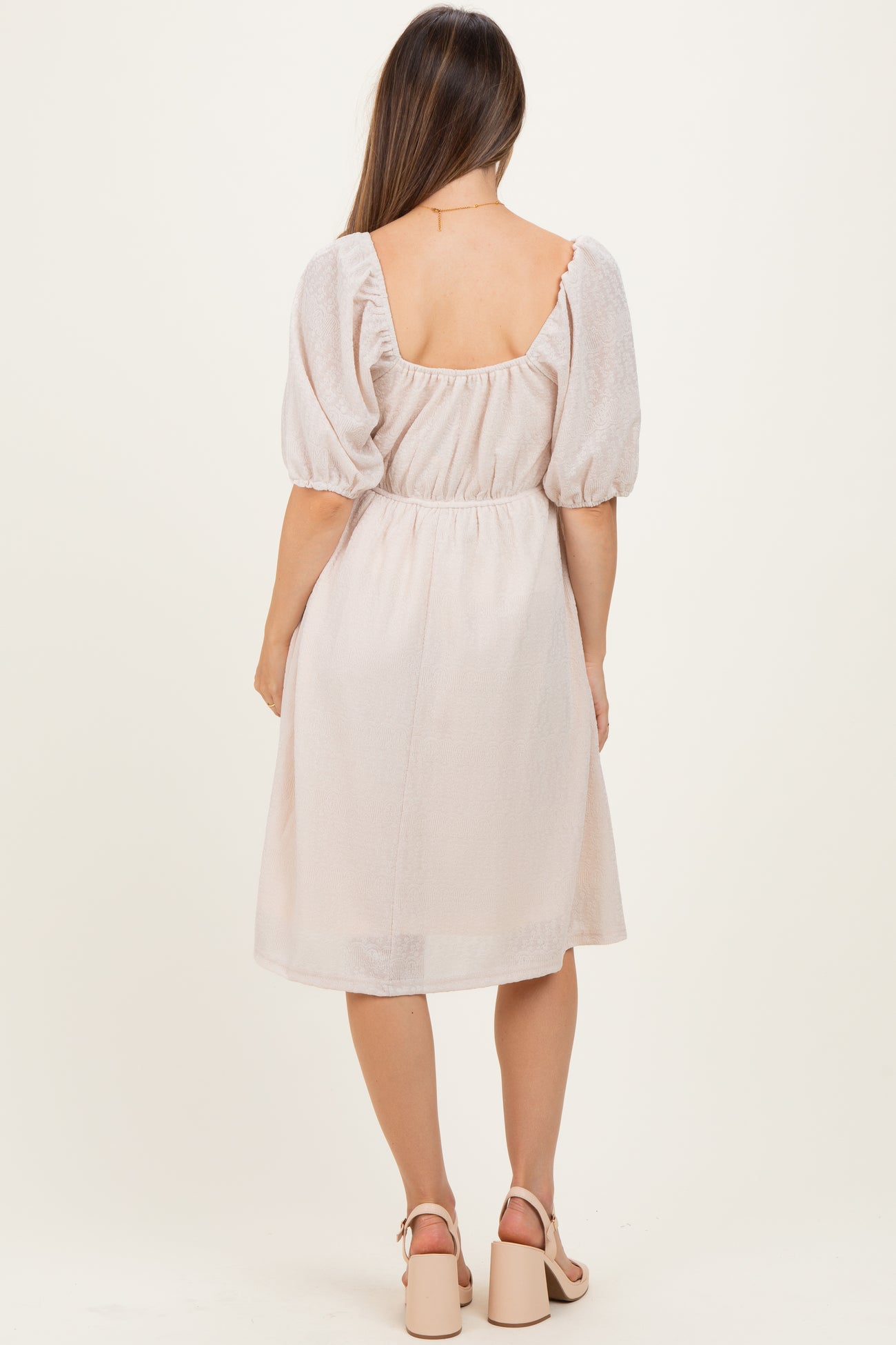 woman wearing a blush pink maternity dress with puff sleeves and a cinched waist, showing her baby bump from the back