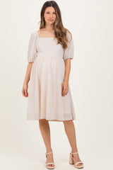 woman wearing a light pink maternity dress with puff sleeves and a square neckline, showing her baby bump
