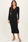 woman wearing a black long sleeve ribbed midi dress with a collar and high slit, standing in a neutral background