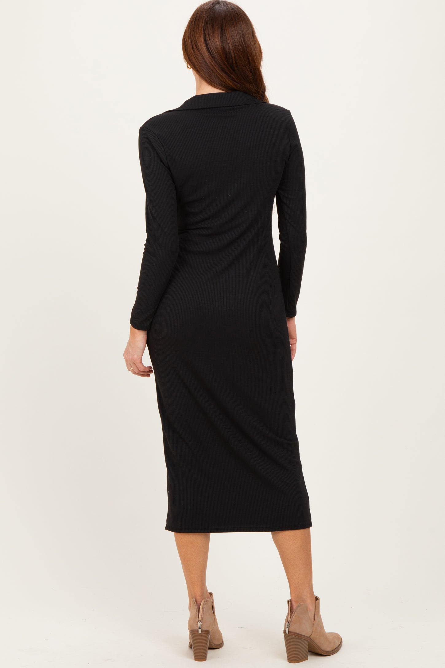 woman wearing a fitted black long sleeve midi dress with a collar and side slit, standing with her back to the camera