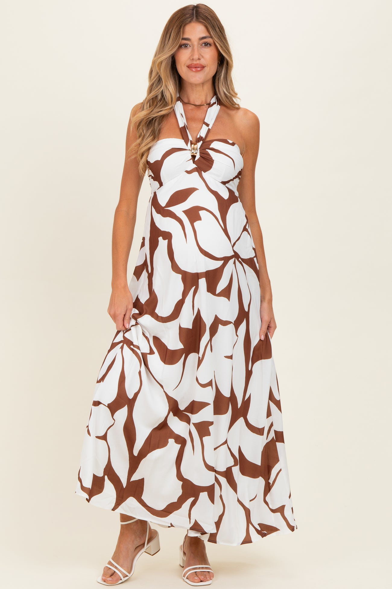 woman wearing a white maternity maxi dress with brown floral print and halter neck detail, and baby bump visible