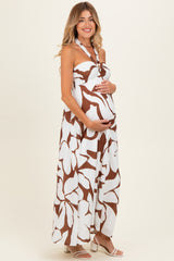 woman wearing a brown and white floral halter maternity maxi dress and holding her baby bump