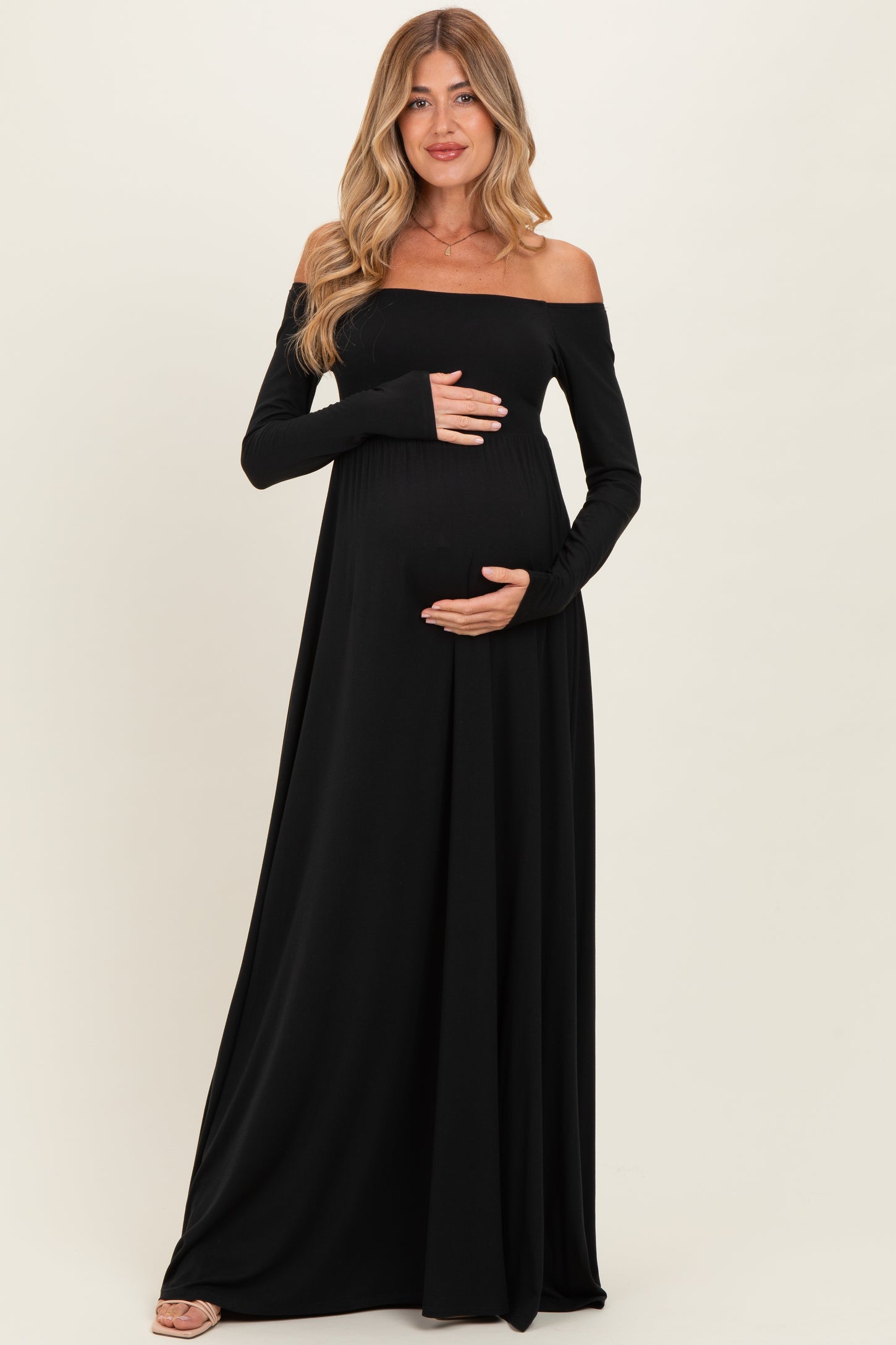 woman wearing a black off-the-shoulder maternity dress and showing her baby bump