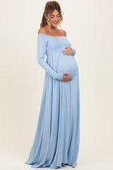 woman wearing a light blue off-shoulder maternity dress with a flowing skirt and holding her baby bump