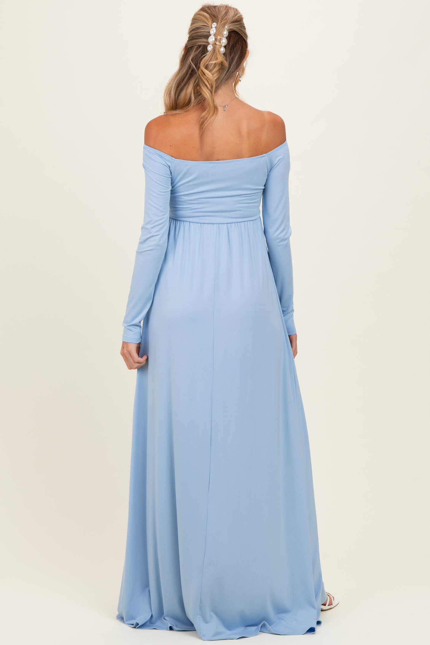 woman wearing a light blue off-shoulder maxi maternity dress with long sleeves and a flowing skirt