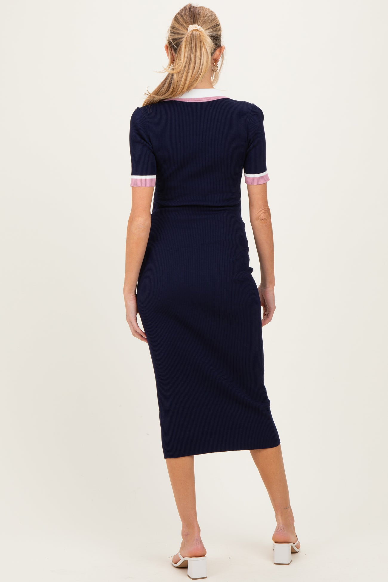 woman wearing a navy blue maternity ribbed dress with pink trim, showing her back and a baby bump