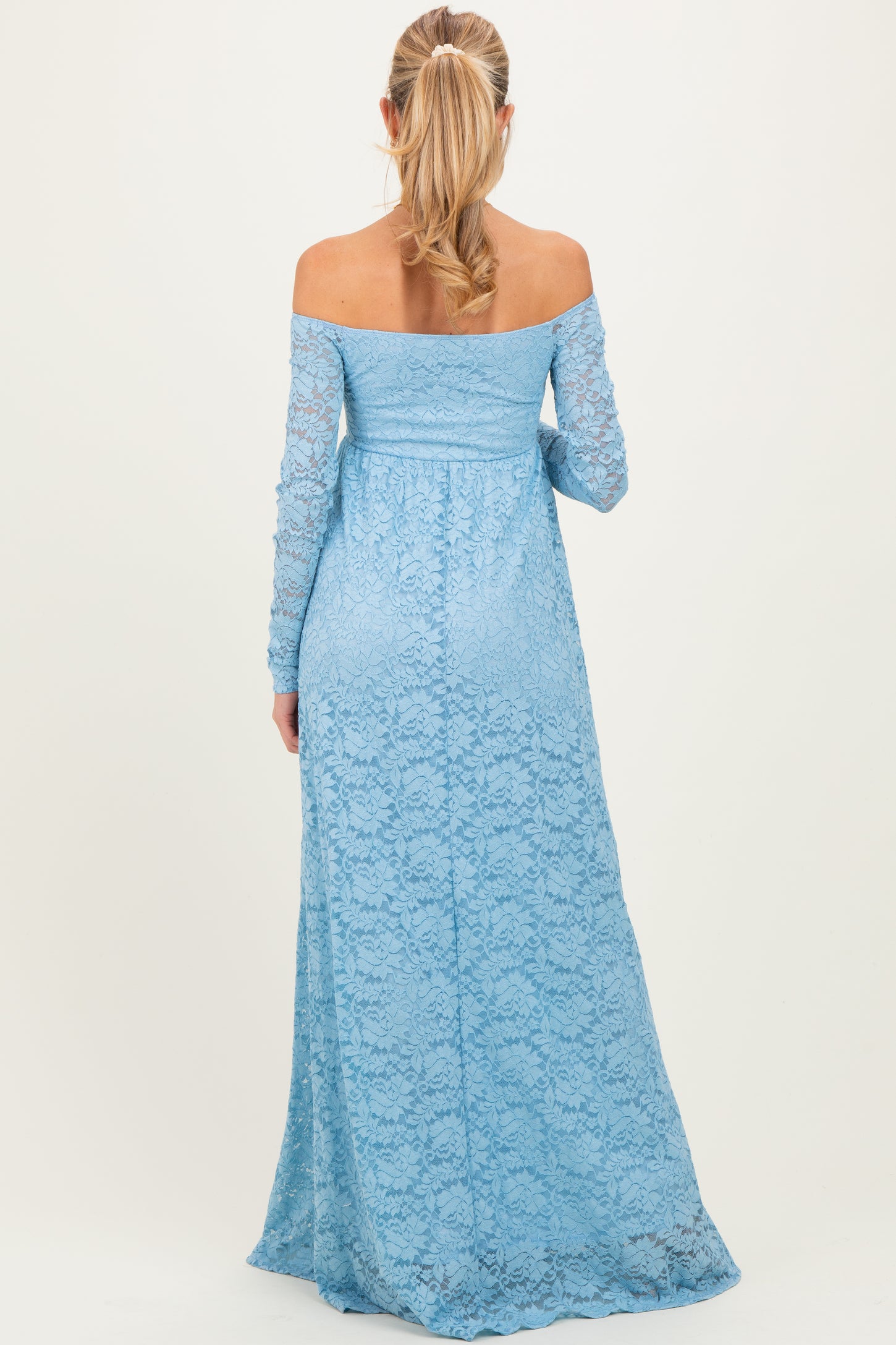 woman wearing a light blue off-the-shoulder lace maternity dress with long sleeves and a flowing skirt
