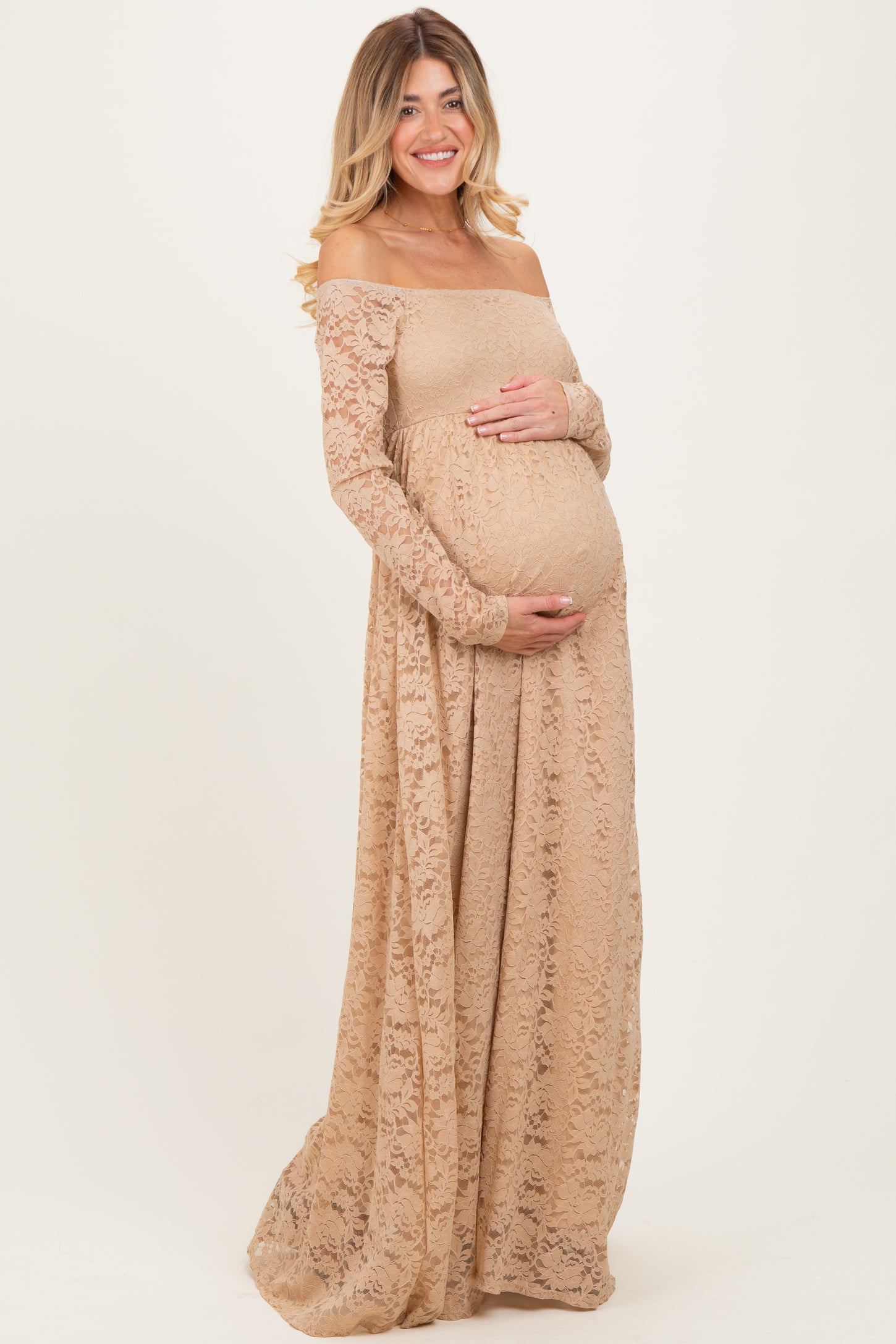 woman wearing a nude off-the-shoulder lace maternity gown and holding her baby bump