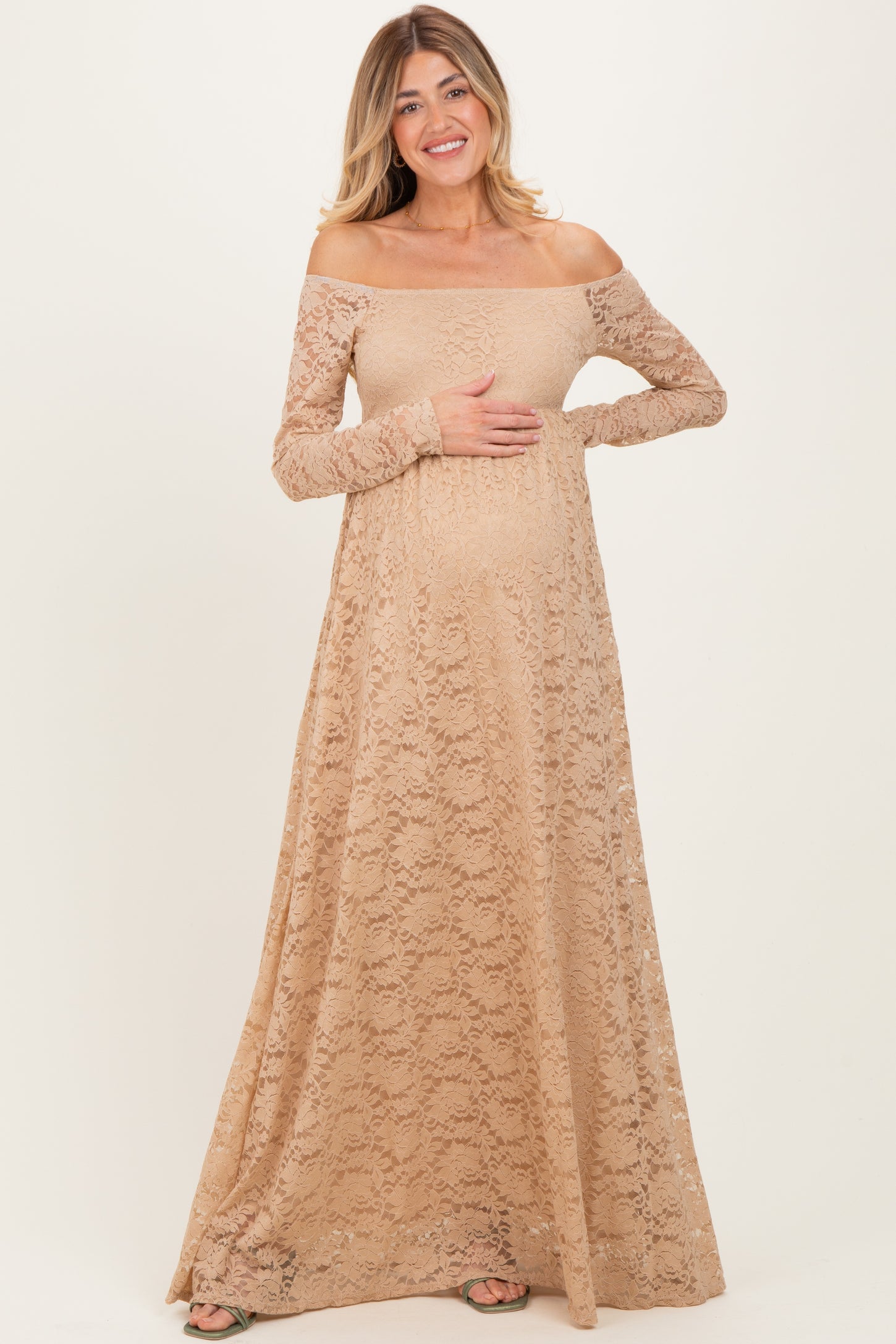 woman wearing a beige off-the-shoulder lace maternity gown and holding her baby bump