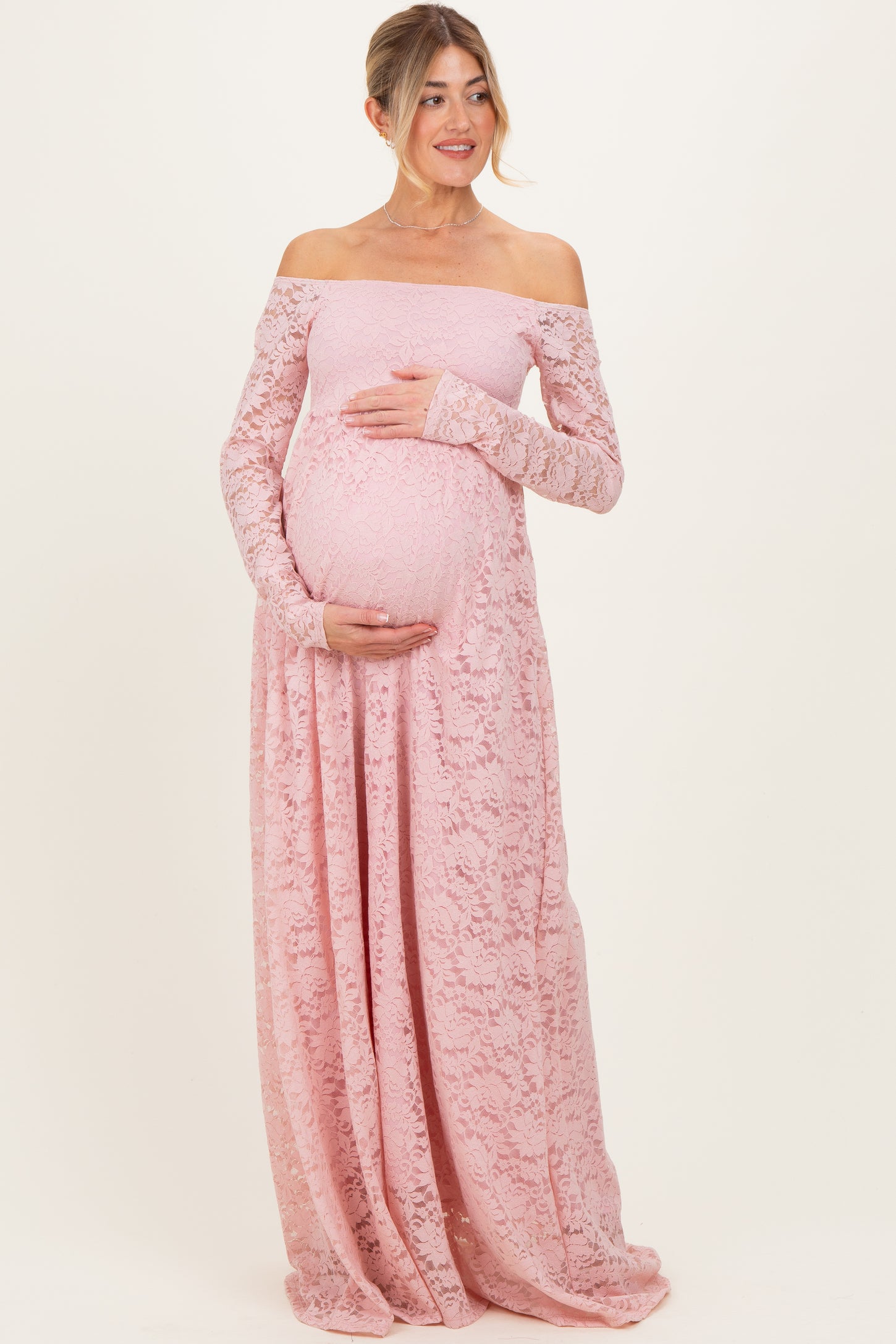 woman wearing a light pink off-the-shoulder lace maternity gown and holding her baby bump