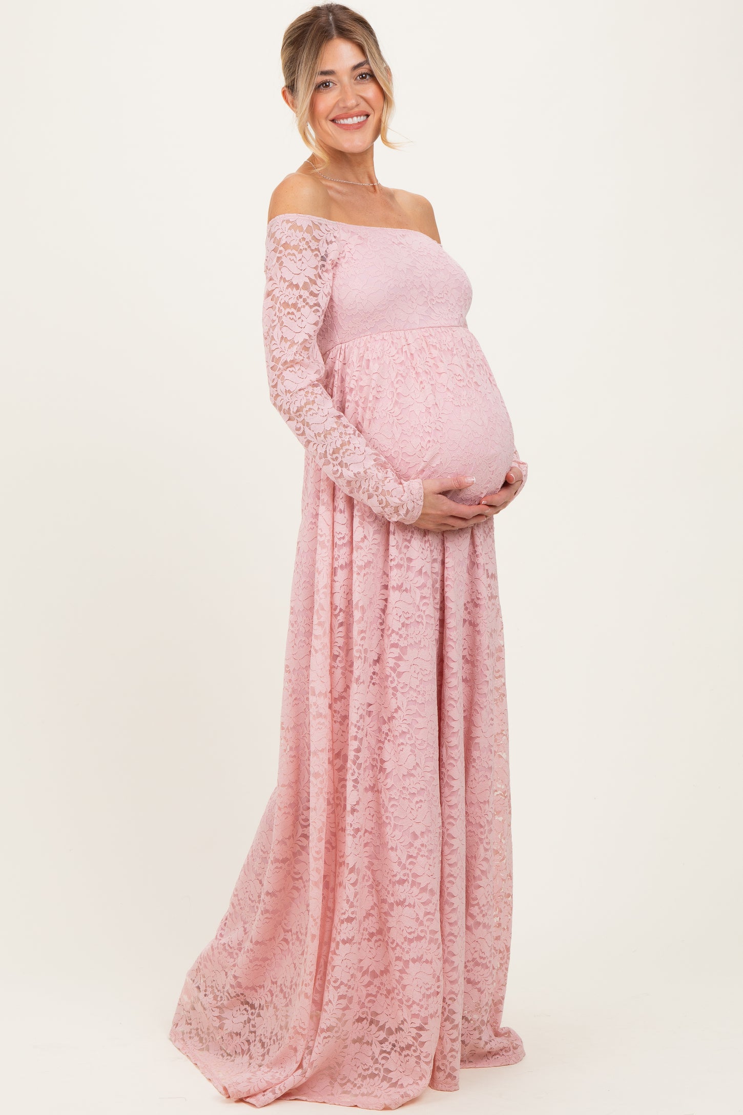 woman wearing a pink lace off-the-shoulder maternity gown and holding her baby bump