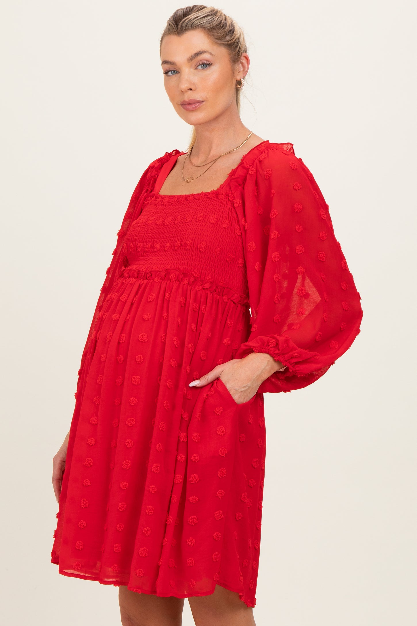 woman wearing a red maternity dress with puff sleeves and smocked bodice, showing her baby bump and featuring pockets
