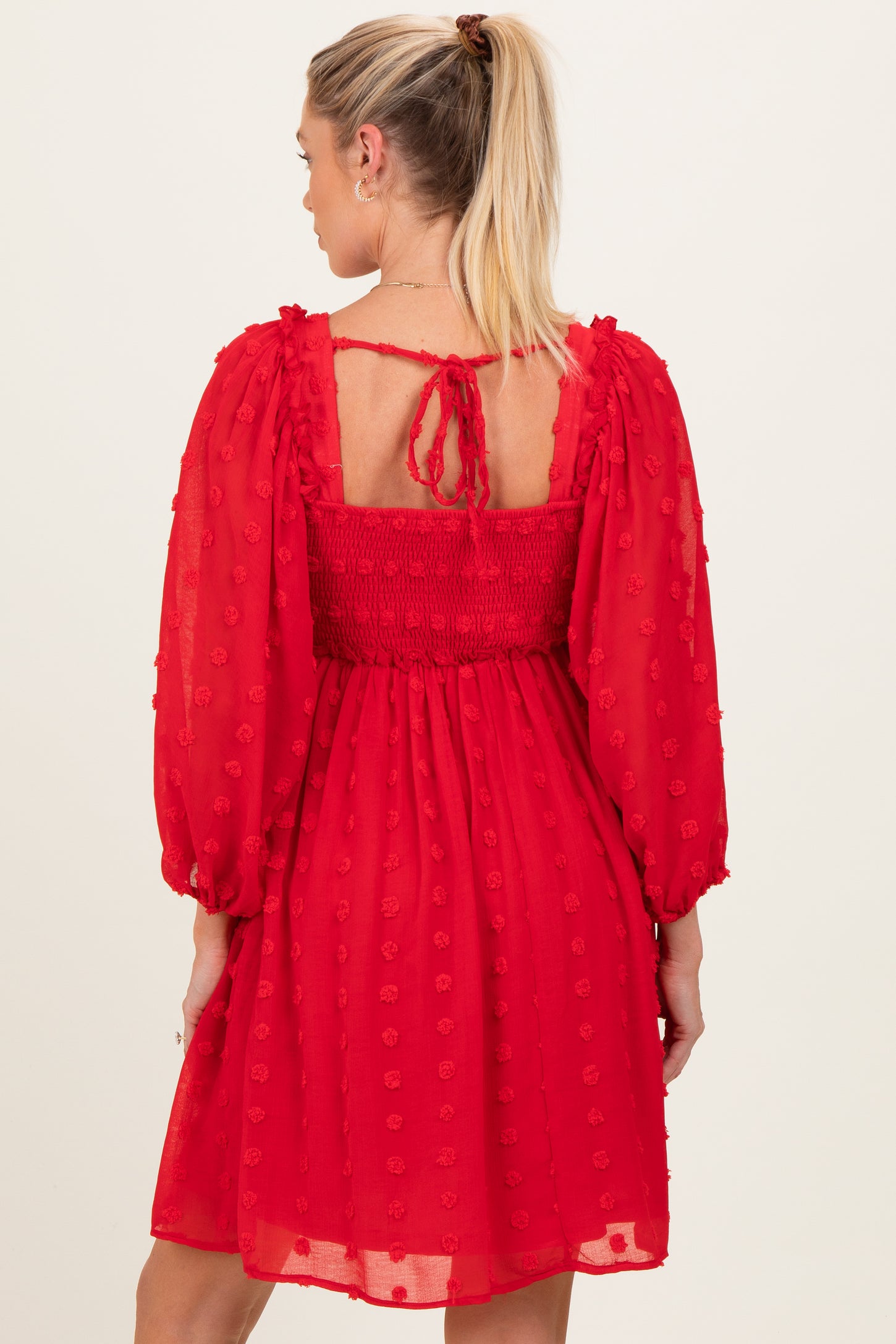 woman wearing a red maternity dress with puff sleeves and a smocked back, featuring textured floral details