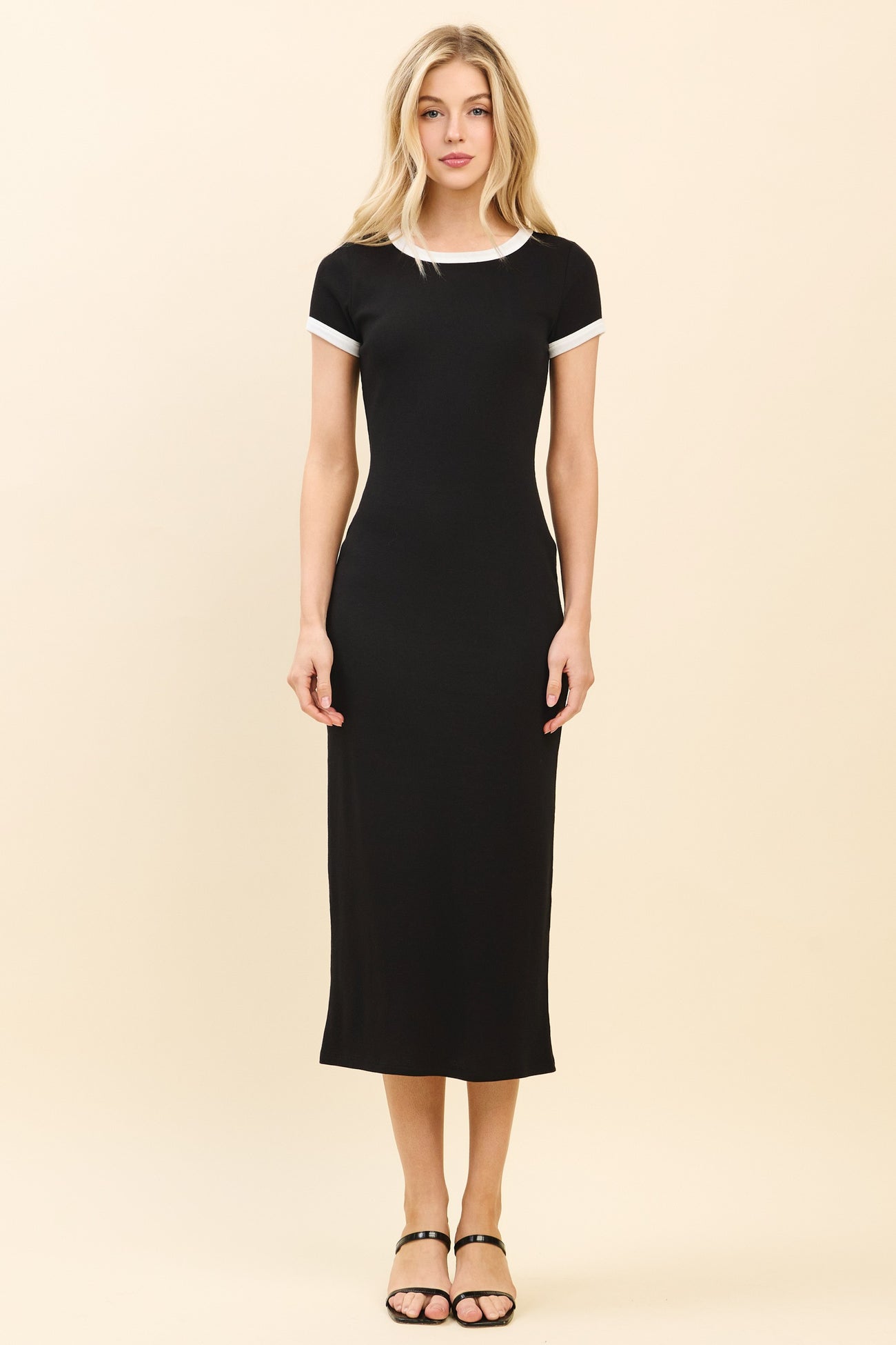 woman wearing a black midi dress with white trim on the sleeves and neckline, standing against a light background