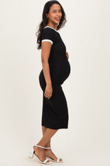 woman wearing a black fitted maternity dress with white trim and holding her pregnant belly
