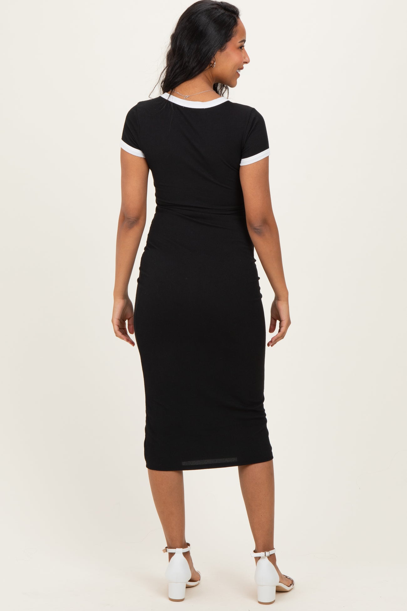 woman wearing a black maternity dress with white trim, showing a fitted style and a visible baby bump from the back