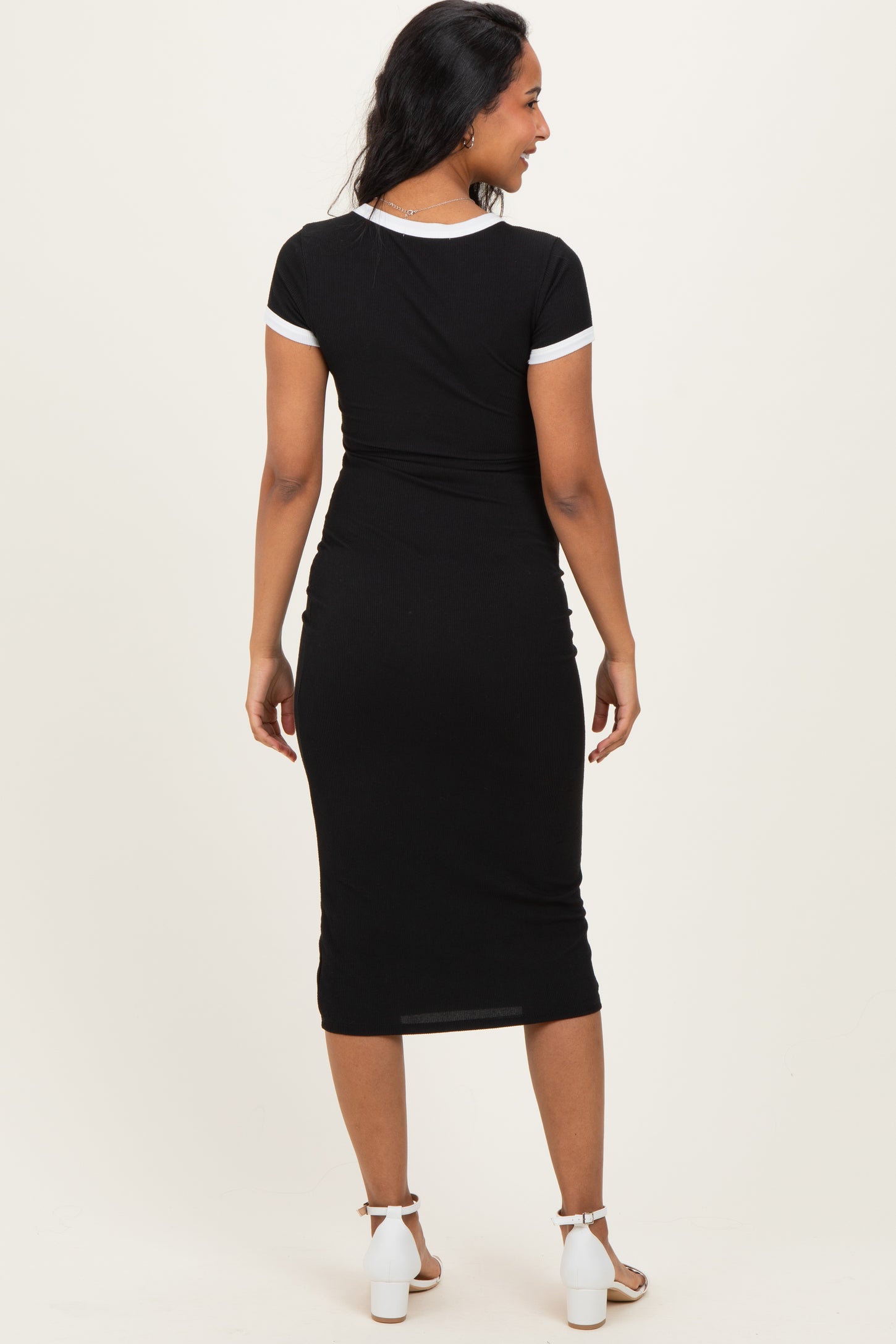 woman wearing a black maternity dress with white trim, showing a fitted style and a visible baby bump from the back