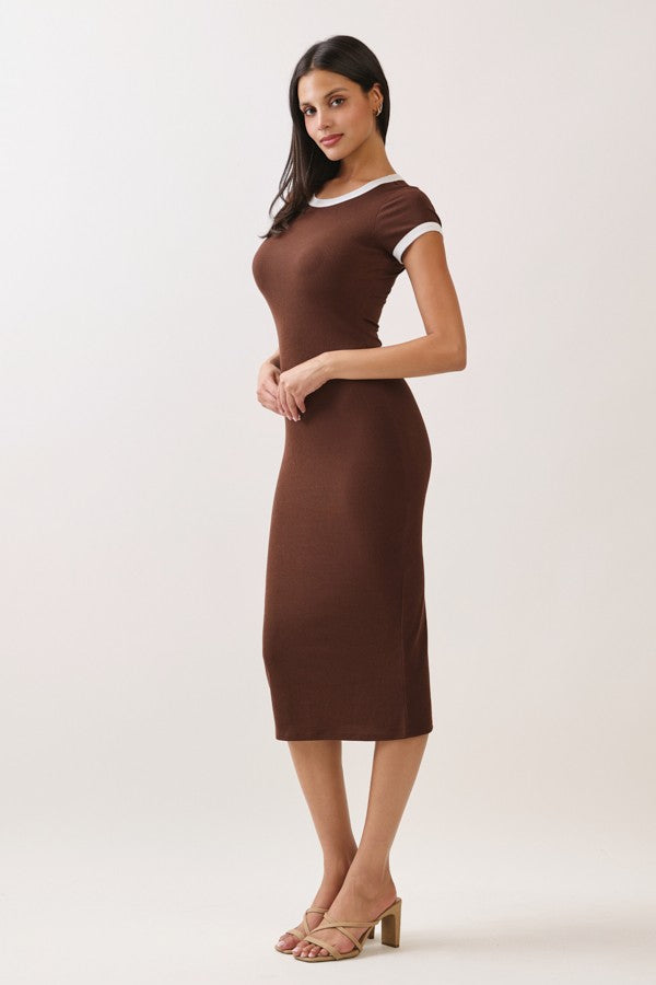 woman wearing a brown fitted midi dress with white trim and strappy heels, standing with hands clasped in front