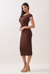 woman wearing a brown fitted midi dress with white trim and strappy heels, standing with hands clasped in front