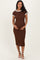 woman wearing a brown ribbed maternity dress with white trim and holding her baby bump