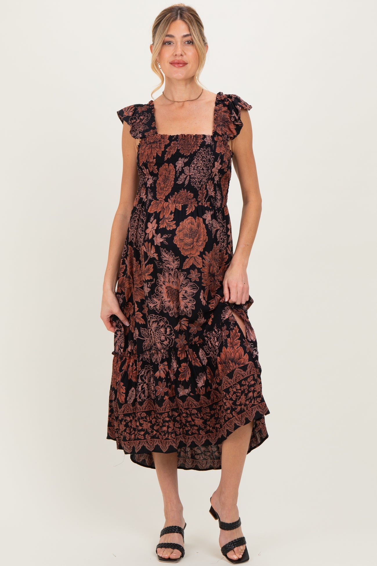 woman wearing a black floral maternity dress with ruffled straps and a midi length, showcasing a baby bump