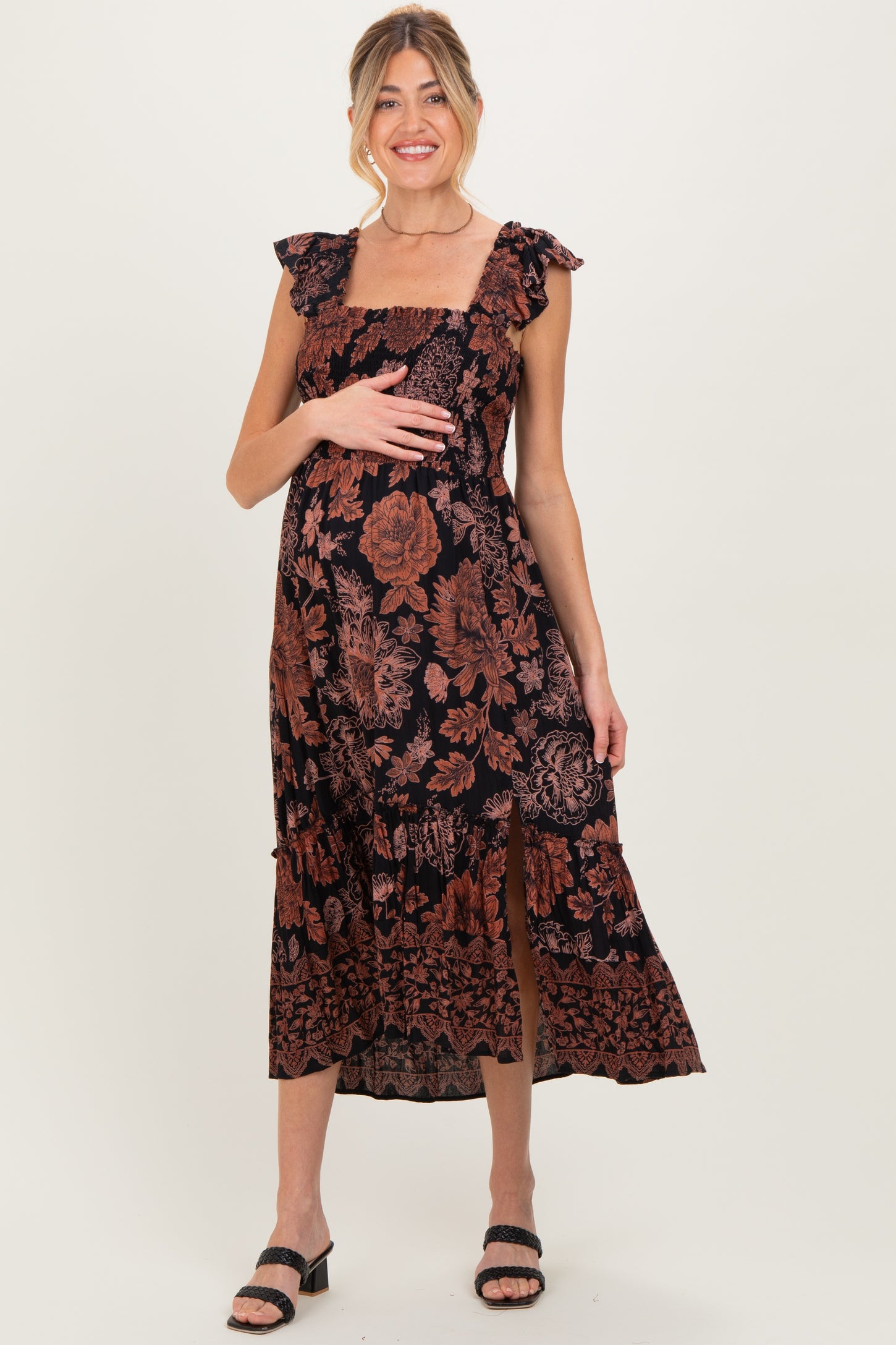 woman wearing a black floral maternity maxi dress with ruffled sleeves and a side slit, holding her baby bump