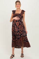woman wearing a black floral maternity maxi dress with ruffled sleeves and a side slit, holding her baby bump