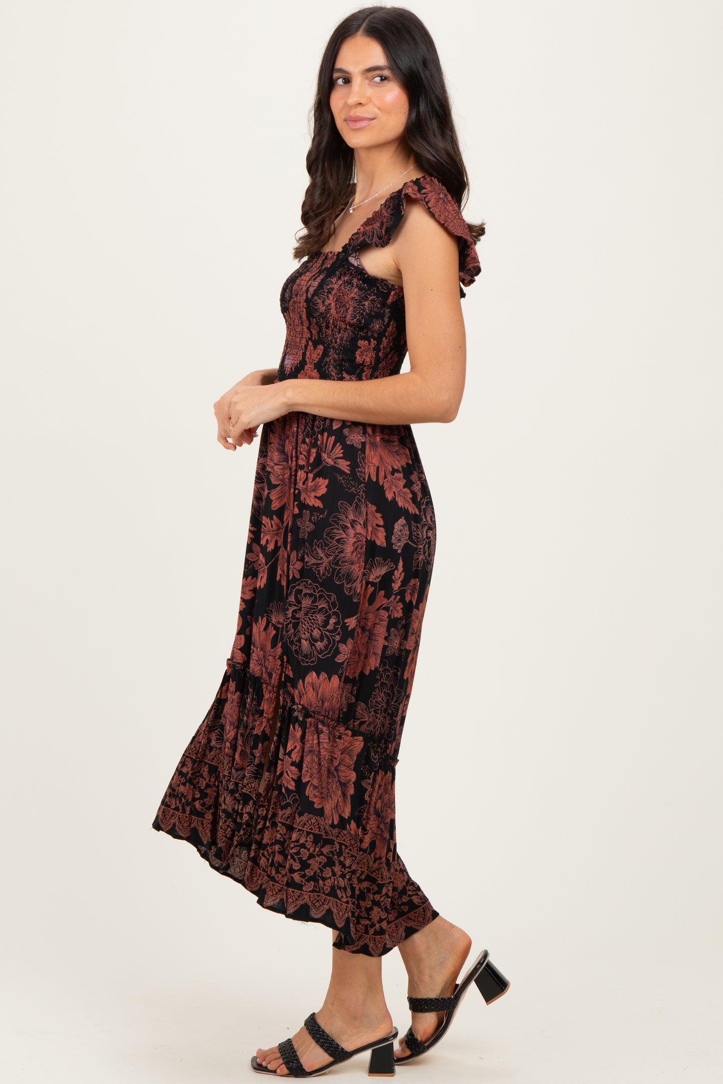 woman wearing a black and rust floral midi dress with ruffled straps and a flowy hem, posed sideways