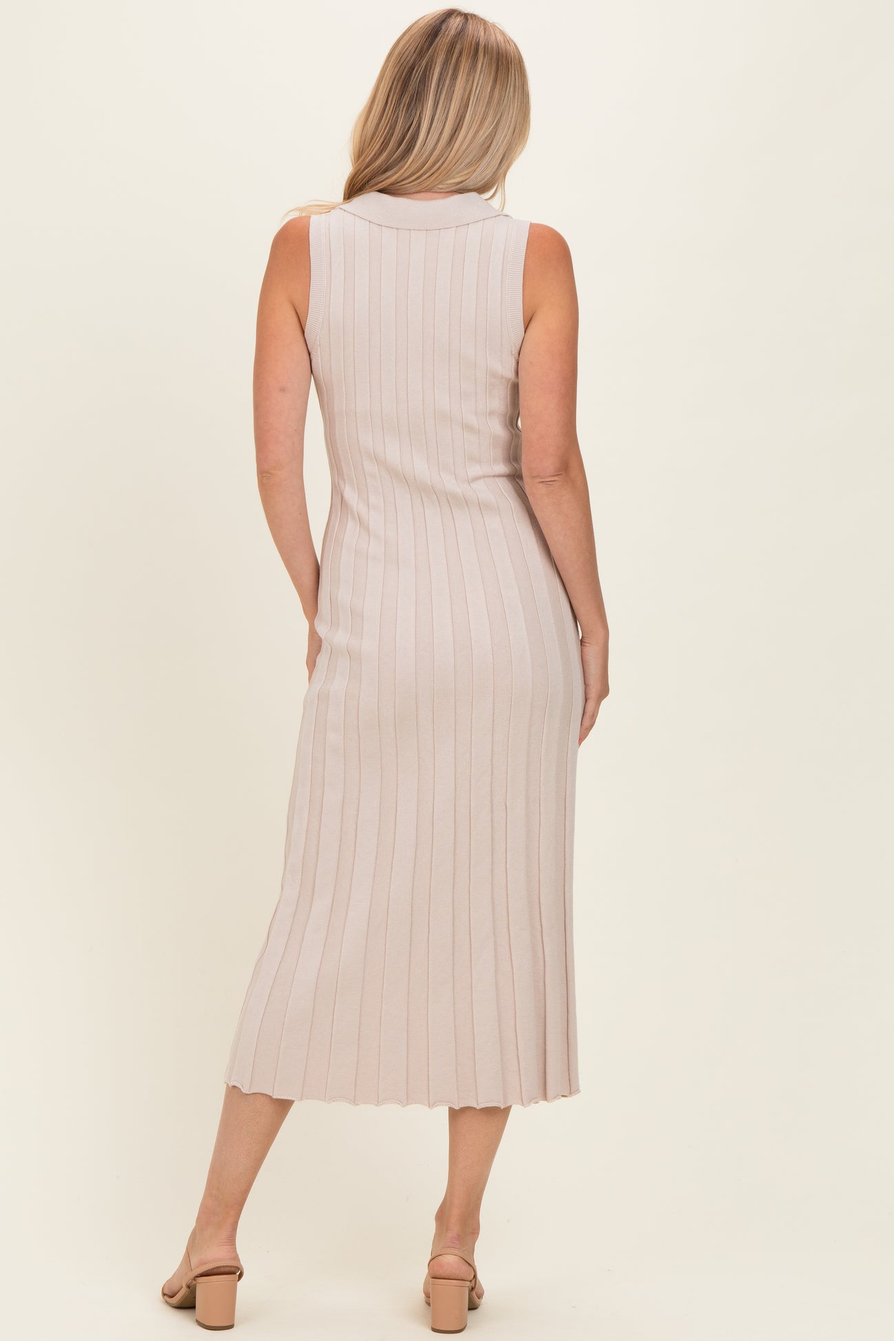 woman wearing a beige sleeveless ribbed midi dress with a fitted silhouette and scalloped hem, viewed from the back
