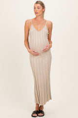 woman wearing a beige ribbed maternity maxi dress with spaghetti straps and cradling her baby bump