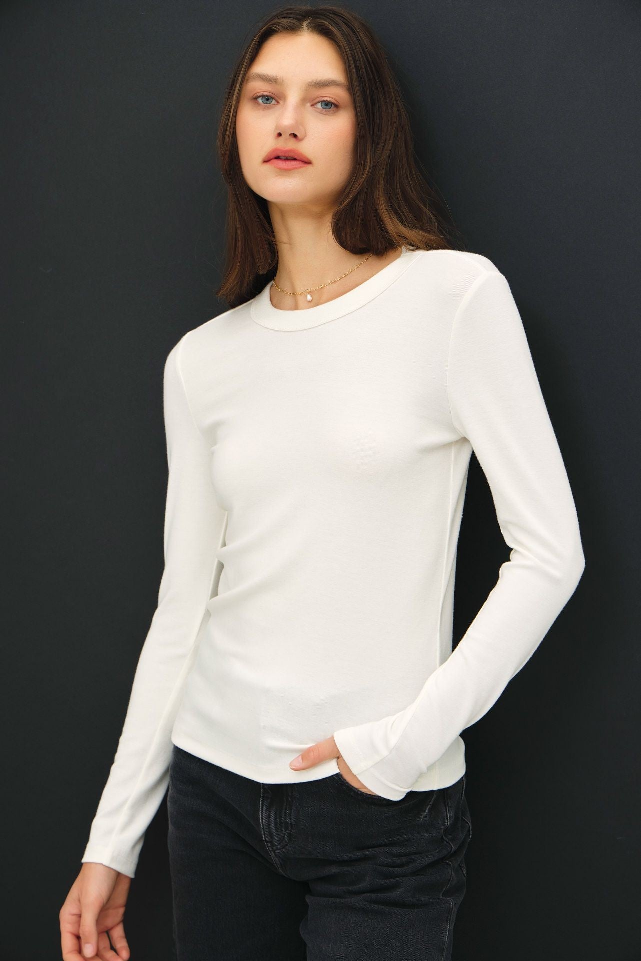 woman wearing a white long sleeve fitted top with a round neckline and black jeans