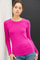 woman wearing a bright pink long sleeve top and blue jeans leaning against a wall