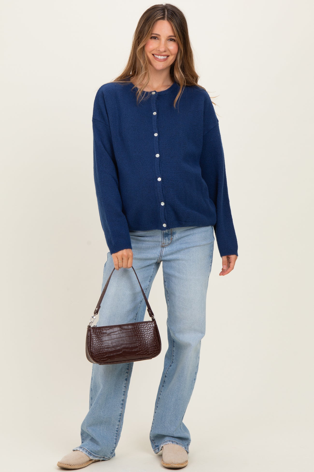 woman wearing a navy blue cardigan with buttons and light blue wide-leg jeans, holding a brown handbag