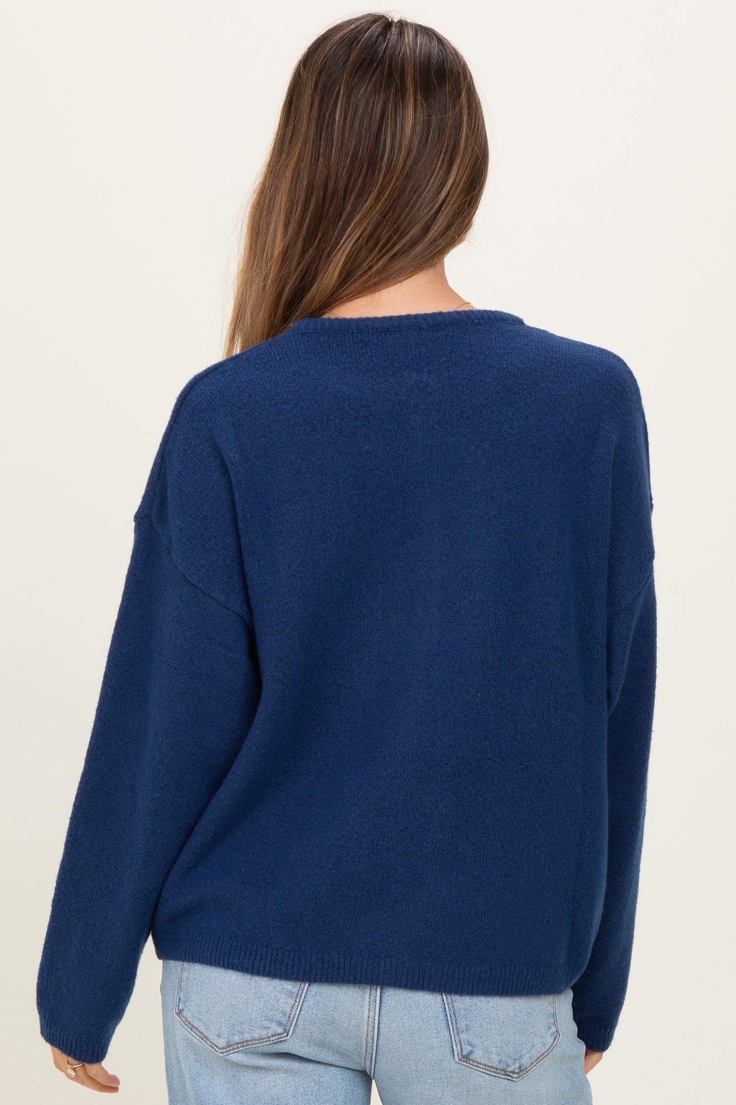 woman wearing a navy blue oversized maternity sweater, seen from the back, paired with light blue jeans