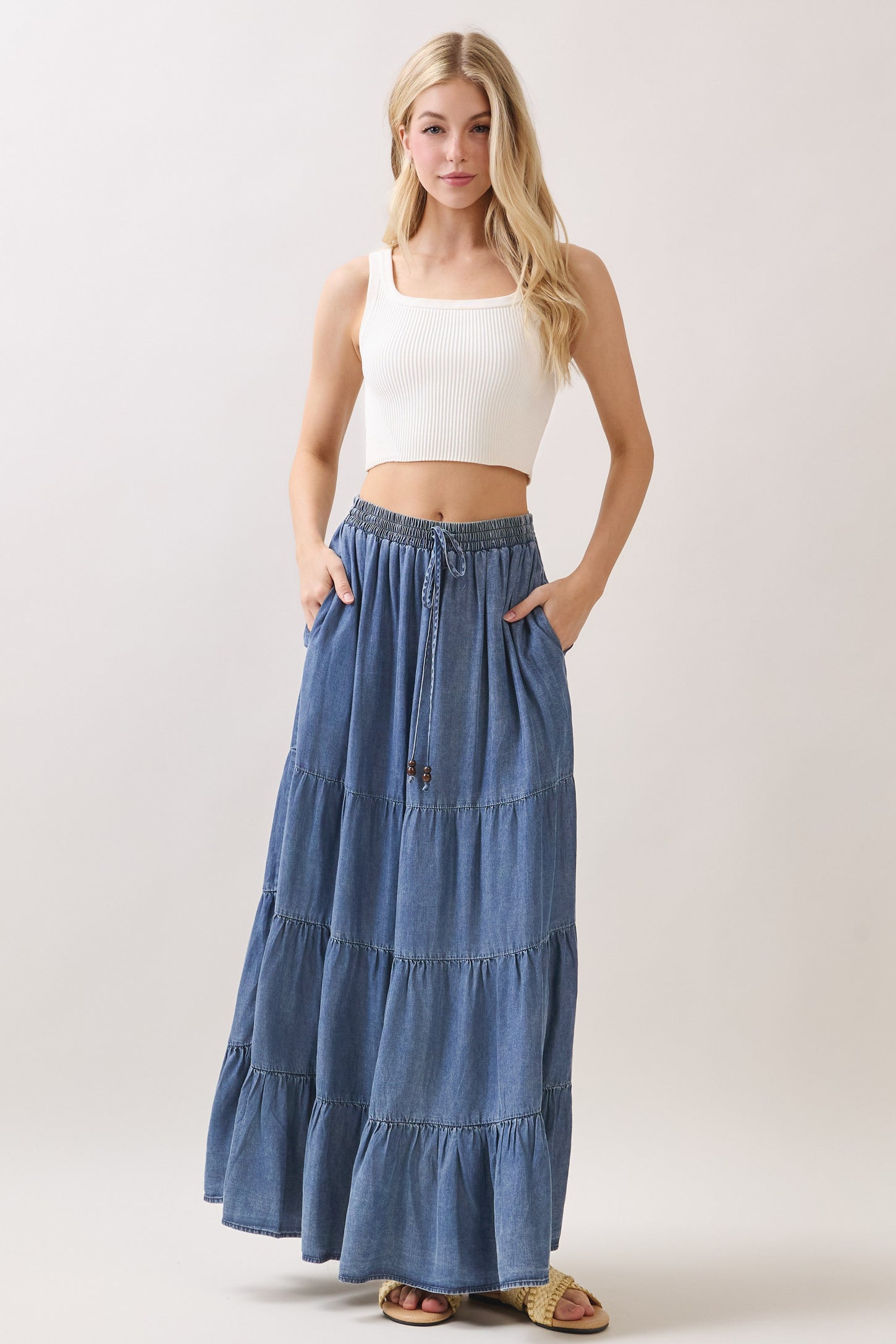 woman wearing a white cropped ribbed tank top and a long denim tiered maxi skirt with pockets