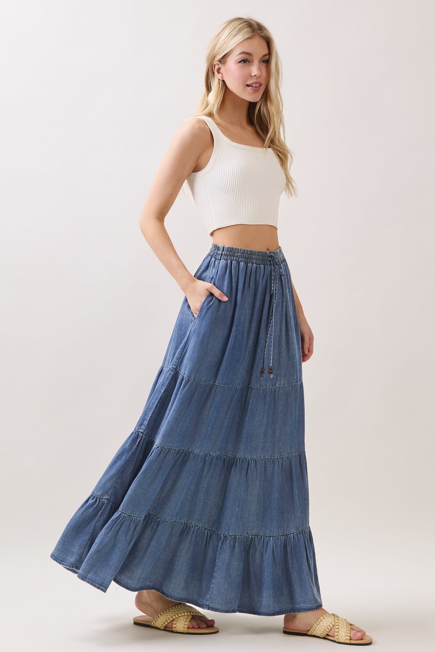 woman wearing a white ribbed crop top and a denim tiered maxi skirt with pockets and a drawstring waist