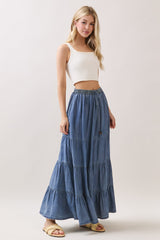 woman wearing a white ribbed crop top and a tiered denim maxi skirt, styled with sandals and casual waves in her hair