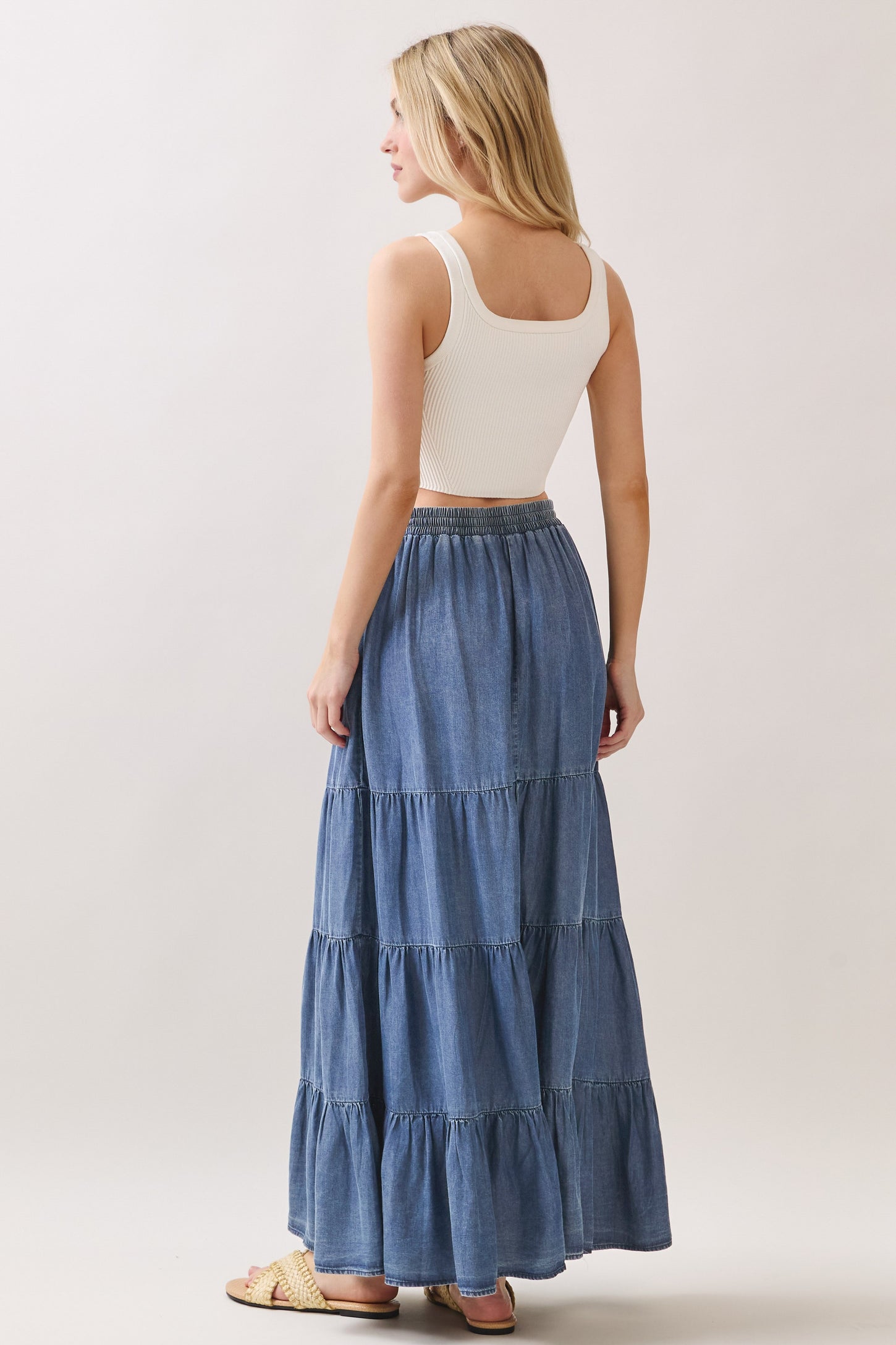 woman wearing a white ribbed tank top and a blue tiered maxi skirt from the back