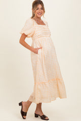 woman wearing a light orange and white gingham maternity dress with puff sleeves and a tiered hem, showcasing her baby bump