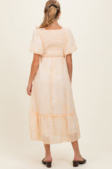woman wearing a peach and white gingham maternity maxi dress with short puff sleeves and a smocked bodice