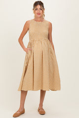 woman wearing a mustard and white gingham maternity dress with a smocked bodice and pockets