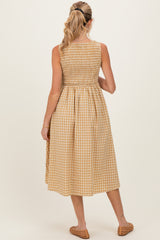 woman wearing a gingham pattern midi maternity dress with a smocked bodice and back pleating, showing her baby bump