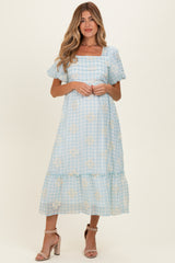woman wearing a light blue maternity dress with puff sleeves and floral pattern, standing against a neutral background