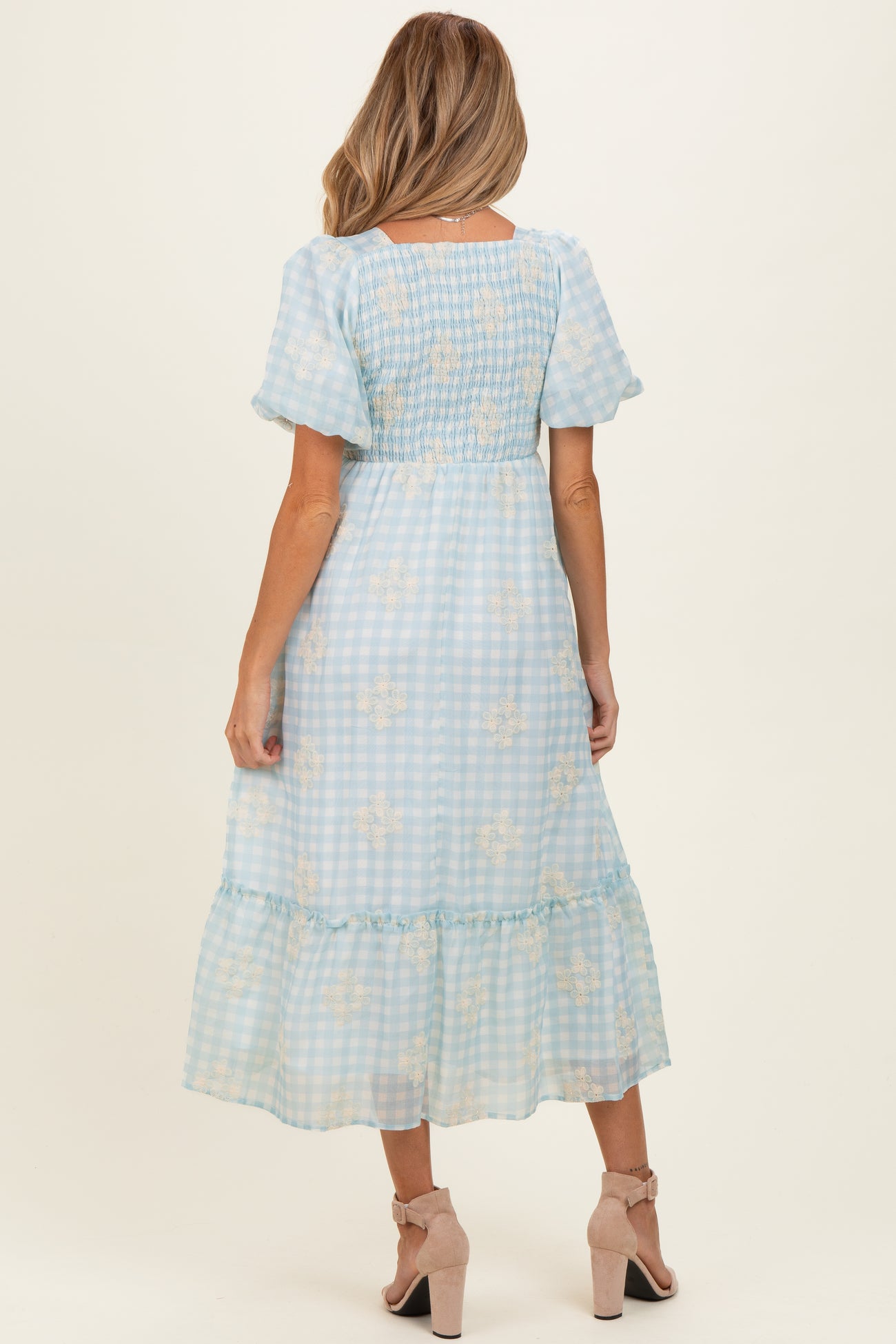 woman wearing a pastel blue gingham maternity dress with floral details and tiered ruffle hem, seen from the back