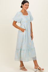 woman wearing a light blue gingham maxi dress with puff sleeves and pockets, styled with white heeled sandals