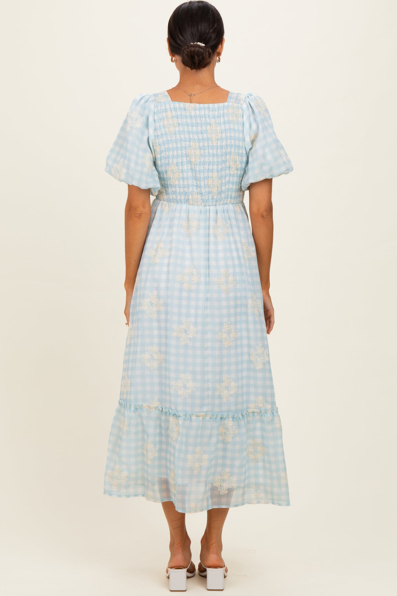 woman wearing a light blue gingham patterned maxi dress with short puff sleeves and floral detailing