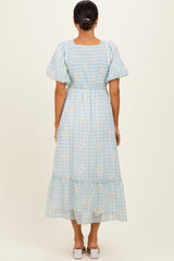 woman wearing a light blue gingham patterned maxi dress with short puff sleeves and floral detailing