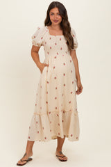 woman wearing a cream floral print maternity dress with puff sleeves and a tiered skirt, showing her baby bump